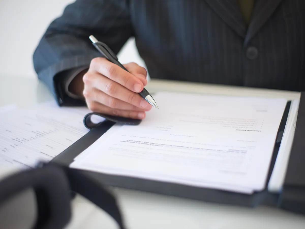 Persona firmando un documento sobre una mesa.